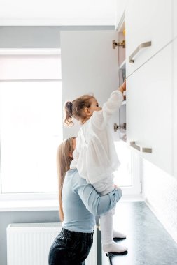 Anne küçük tatlı kızını mutfakta tutuyor. Genç, şefkatli bir anne ve heyecanlı bir kız ailesi.