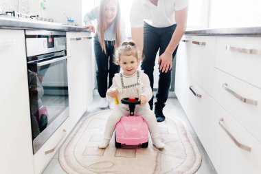 Amerikalı ebeveynler, evlerinin penceresinin yanındaki pembe arabanın üzerinde kızlarıyla eğleniyorlar. Tek çocuklu geleneksel aile