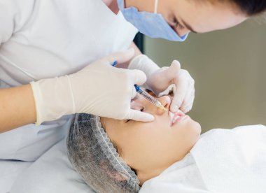 Güzellik uzmanının ellerinin kadın dudaklarına iğne yaptığı yakın çekim görüntüsü. Güzel bir muamele olarak dudaklarına enjekte edilen kadın. 