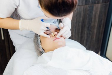 Güzellik uzmanının ellerinin kadın dudaklarına iğne yaptığı yakın çekim görüntüsü. Güzel bir muamele olarak dudaklarına enjekte edilen kadın.