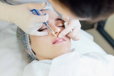 Kadın dudaklarına kozmetik enjeksiyonunu kapat. Kozmetik uzmanının özel sıvıyla şırınga kullanması ve hastaların çenesini tutması, kozmetoloji kavramı, güzellik.