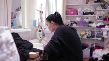 Genç bir kadın atölyede profesyonel bir makineyle dikiş dikiyor. Profesyonel terzi, özgün bir imaj. Dikiş makinesinin yanındaki giyim tasarımcısı,