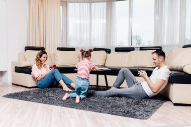 Mutlu çocuk evde yerde çocuk çizim setini kullanarak birlikte oynuyor. Yatay görüntü. Küçük kız, sıcak zeminde çizim yapıyor. Ebeveynler kanepede dinleniyor.,