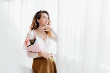 Beyaz bluz giymiş genç bir kadının ellerinde pembe lalelerden oluşan bir buket var. Güzel bir annenin elinde tutulan pembe çiçekler. Poz ver ve Anneler Günü 'nü kutla