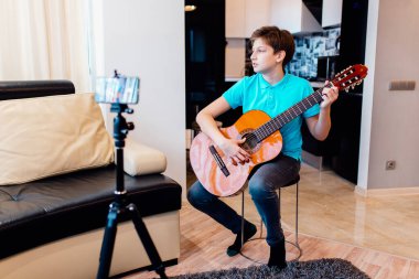 Beyaz tenli genç gitar çalıyor, Online Gitar Dersleri alıyor, en sevdiği hobiyi yapıyor, boş vakit geçiriyor. Kafkas çocuk video aracılığıyla arkadaşlarıyla çevrimiçi müzik çalmak için sanal mutlu saatler buluşması.