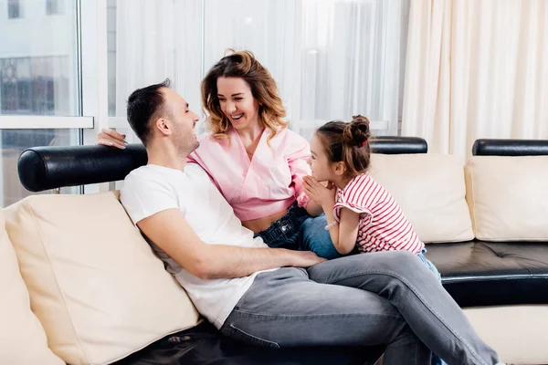 Çocuk ve ebeveynler arasındaki ilişki. Baba ve anne, kızları onlara yalvarırken gülümsüyor. Rahat kanepeye otur. Mutlu aile karantinada kalır..