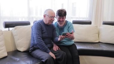 Bir çift son sınıf öğrencisi gülümsüyor ve aynı akıllı telefona bakıyor. Kanepede kucaklaşıyorlar.