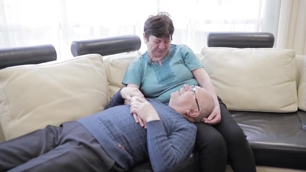 Idős pár pihenő kanapén, békés jelenet. Idősebb fehér férfi feküdjön le a kanapéra a nagymamával — Stock videók