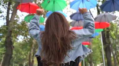Asılı şemsiyelerle parkta zıplayan mutlu kadın.