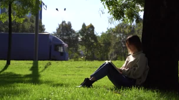 Dışarıda kitap okuyan genç bir kız. Çayırdaki yeşil çimlerde oturuyor.. — Stok video