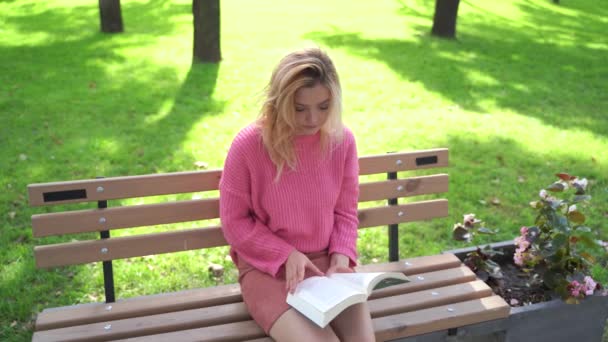 Girl in pink sweater reading a book — Stock Video