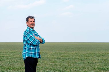 Kıdemli bir çiftçinin tarlada ekinleri incelerken ellerini çaprazlamasına bakıyorum..
