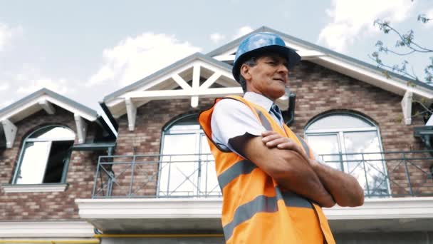 Construtor masculino empreiteiro fica com as mãos cruzadas sorrindo e olhando para longe. — Vídeo de Stock