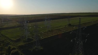 İHA, gün batımında yüksek voltajlı bir elektrik hattını destekleyen bir aktarım kulesinin üzerinde uçuyor..