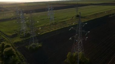 İHA, gün batımında yüksek voltajlı bir elektrik hattını destekleyen bir aktarım kulesinin üzerinde uçuyor.