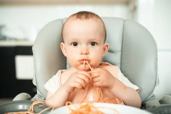 Carino piccolo ragazzo mangia spaghetti con gusto e ottiene sporco con rosso sous — Foto Stock