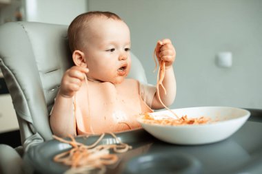 Küçük tatlı çocuk spagettiyi zevkle yiyor ve kırmızı sousuyla kirleniyor.