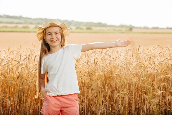 Портрет усміхненої дитини з капелюхом, що стоїть на пшеничному полі з витягнутими руками . — стокове фото