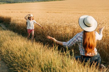 Kafasında şapkasıyla küçük mutlu bir kız annesine koşuyor buğday tarlasının yanında