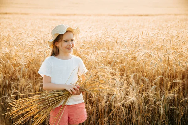 Niña feliz con sombrero sostiene espigas de trigo en sus manos. —  Fotos de Stock