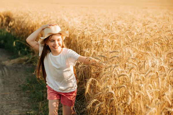 Adorable niña corre felizmente en el camino cerca del campo de trigo amarillo. —  Fotos de Stock