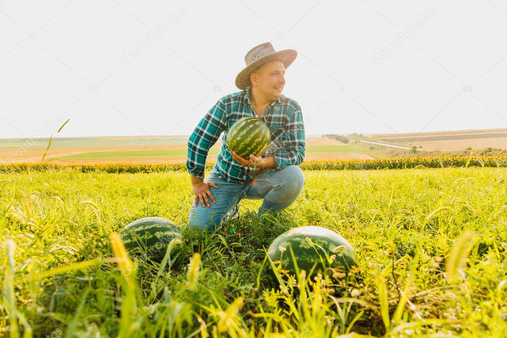 farmer smiles and looks at the camera, holding a big watermelon in his hand.