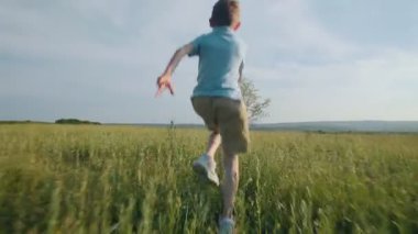 Uzun yeşil çimlerin arasında koşan bir çocuğun arka görüntüsü. Açık havada çocukluğun neşesini ve saf özgürlüğünü kutlayan güzel, poz verilmemiş bir an..
