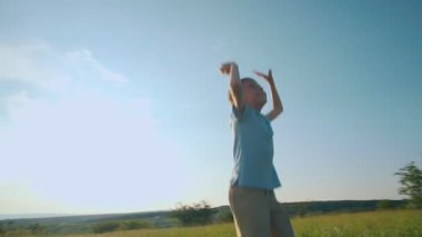 Gülümseyen ve hayat dolu genç bir çocuk güneşli bir günde havaya sıçrıyor, kolları çimenli bir tarlaya doğru uzanıyor çocukluğun özü ve filtresiz bir sevinç..