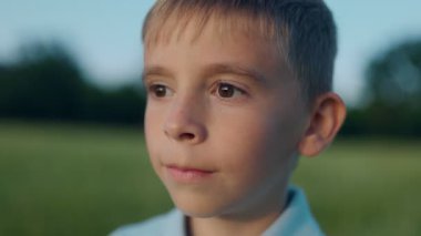 Dışarıdaki genç bir çocuğun portresi, barışçıl ve yansıtıcı bir duygu gösteriyor. Arka plandaki yumuşak ışıklandırma ve alan sakin ve doğal bir his yaratıyor..