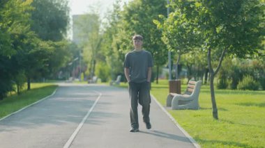 Elleri ceplerinde şehir parkında yürüyen genç bir adam, tüm vücudunu ele geçirmiş. Sakin ifade, güneş ışığı ve ağaçlar gevşemiş gençlik enerjisini vurgular.