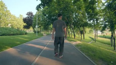 Genç bir çocuğun ağaç gölgelerinin altında parkta tek başına yürüdüğünü gördüm. Şehir sakinliği, gençlik yansıması, kişisel alan ve barışçıl açık hava anı..