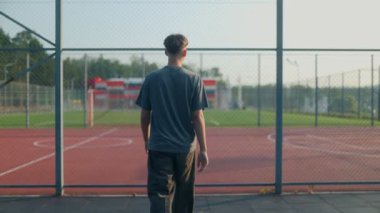 Back view of a teen walking to the basketball court as the sun sets. A calm, reflective sports moment with vibes of freedom, youth, and personal space.