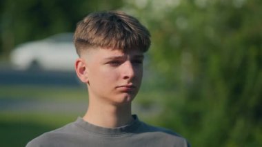 Açık havada genç bir çocuğun yakın çekimi, ciddi bir bakışla düşünceli bir şekilde uzaklaşıyor. Doğal ışık, yaz yeşillikleri, ve karamsar, yansıtıcı titreşim anı yakala..