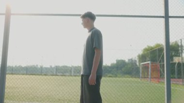 Gündelik giysiler içinde genç bir çocuk sessiz bir açık hava basketbol sahasının önünden yavaşça geçer. Sahne, kurnaz yaz gölgeleri ve sakin titreşimlerle serin bir hava yakalar..