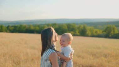 Neşeli bir anne, güneşli bir günde gülen bebeğini havaya kaldırır. Aralarındaki bağ ve tasasız neşe mavi gökyüzünün altında parıldıyor..
