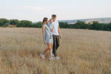 Genç bir aile gün batımında altın bir tarlada geziniyor. Anne bebeğini kucağında tutarken, baba onların yanında yürüyor, sakin ve sevgi dolu bir anın tadını çıkarıyor..