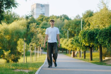 Genç bir çocuk sessiz bir şehir parkında tek başına yürüyor, elleri cebinde, düşüncelere dalmış. Huzurlu bir an. Ruh hali, içgözlem ve gençlik havası..
