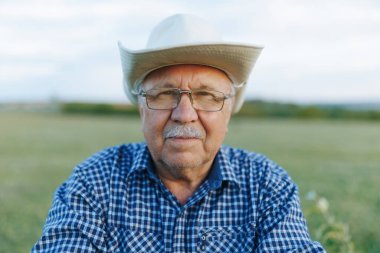 Amerikalı bir kovboy çiftçi gün batımında ellerini bir sopayla dinlendirip toprağının üzerindeki mesafeye bakıyor. Sakin ve deneyimli bir güçle ayakta duruyor..