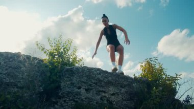 Odaklanmış genç bir kadın doğadaki bir egzersiz sırasında dik kayalık bir tepeye tırmanır. Onun gücü, azmi ve cesareti her güçlü hareketi yokuş yukarı gösteriyor..