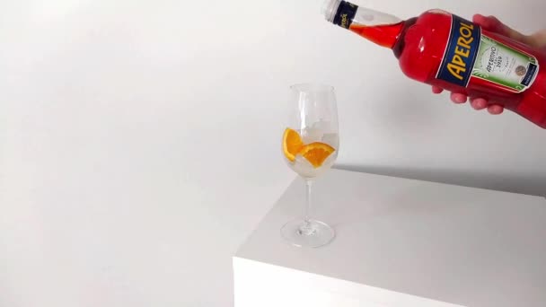 Lugansk, Ucrânia - 29 de março de 2021: Making an Aperol Spritz Cocktail. Mulher mão derramando aperol em copo de vinho com gelo — Vídeo de Stock