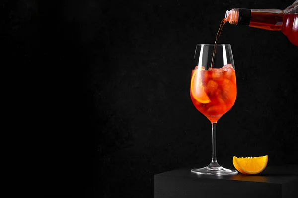 Verser Aperol Spritz Cocktail dans un verre à vin avec de la glace et une tranche d'orange sur fond sombre. Longue boisson gazeuse — Photo