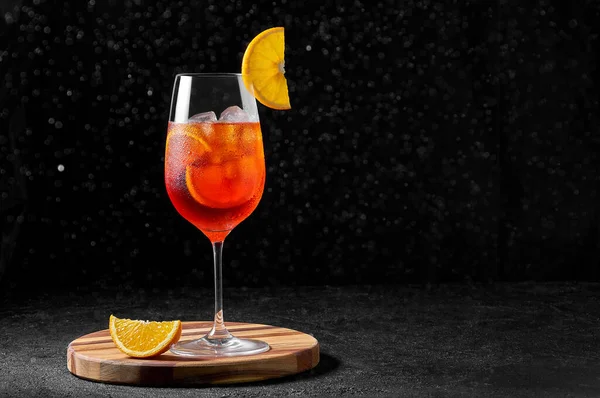 Aperol Spritz Cocktail em copo de vinho com água salpicante em tábua de madeira sobre fundo escuro. Bebida longa e gasosa — Fotografia de Stock
