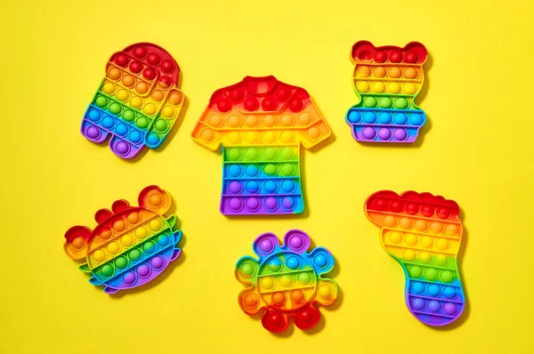 Trendiges Pop-it-Spielzeug in Form von T-Shirt, Fuß, Krabbe, Bär, Blume und einer Figur unter uns auf gelbem Hintergrund. — Stockfoto