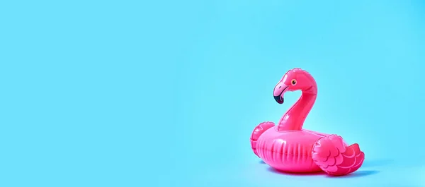 Inflatable pink flamingo pool toy on blue background. Creative minimal concept. Banner.