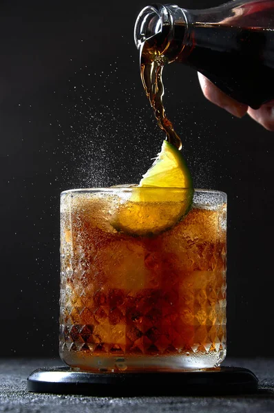 Cuba Libre o Long Island Cocktail con cola, ron y lima en vaso. Spray de soda sobre fondo oscuro. Refrescante bebida de verano Imagen de stock