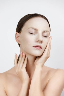 Yüz bakımı Kore kozmetik ürünlerini nemlendiriyor. Sağlıklı Taze Cilt Üzerine Beyaz Maske Uygulayan Güzel Kadın Portresi. Yüz derisindeki kumaş maskesi. Yüksek Çözünürlük
