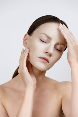 Yüz bakımı Kore kozmetik ürünlerini nemlendiriyor. Sağlıklı Taze Cilt Üzerine Beyaz Maske Uygulayan Güzel Kadın Portresi. Yüz derisindeki kumaş maskesi. Yüksek Çözünürlük