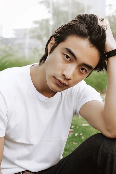 Asian male model posing, long dark haircut, wearing watch and white t-shirt, park, outdoors, model test shoot, student lifestyle, looking in the camera, straightens hair with hand