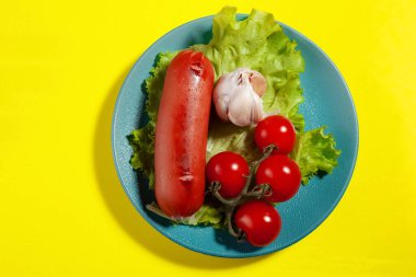 Kızarmış sosis, lezzetli vişneli domates, marul ve sarımsak, sarı bir arka planda.