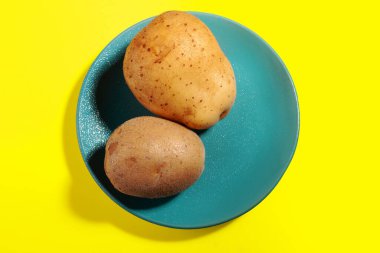 Mavi tabakta iki çiğ patates, sarı arka planda.